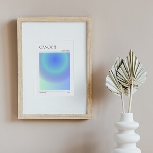 May include: A framed print with a light blue, green, and white gradient design. The print has the word "CANCER" in black text at the top and the dates "June 21 - July 22" in smaller black text below. The words "Zodiac Sign" and "Water" are in smaller black text at the bottom of the print.