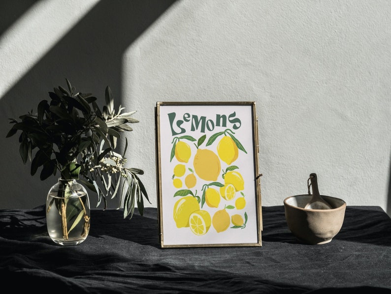 May include: A framed print with a yellow and green illustration of lemons and the word "Lemons" in a retro font. The print is sitting on a black surface with a small bowl and a spoon.