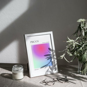 May include: White frame with a colorful gradient print inside. The print has the word "Pisces" and the dates "February 19 - March 20". The frame is sitting on a light brown surface with a candle and glasses.