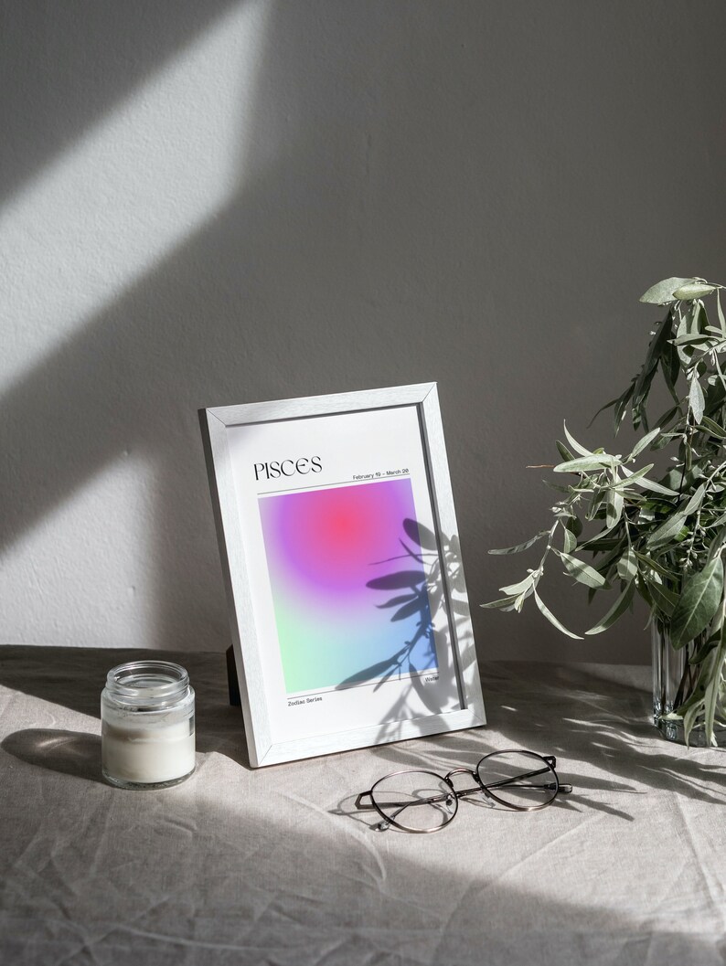 May include: White frame with a colorful gradient print inside. The print has the word "Pisces" and the dates "February 19 - March 20". The frame is sitting on a light brown surface with a candle and glasses.