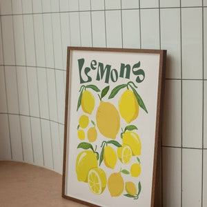 May include: A framed print with the text "Le Mons" in green lettering and a white background. The print features a cluster of yellow lemons with green leaves.