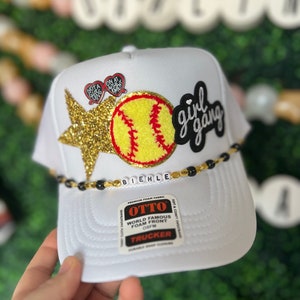 May include: White trucker hat with a gold star, a softball, and a black and white patch that says "girl gang". The hat also has a black beaded trim and a label that says "OTTO World Famous Foam Front OSFM Trucker".