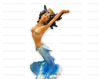 Könnte beinhalten: Eine Figur von Yemaya, einer Meerjungfrau mit brauner Haut, schwarzen Haaren und einer goldenen Krone. Ihr Schwanz ist blau mit einem Schuppenmuster, und sie taucht aus blauen Wellen auf. Auf dem Sockel der Figur steht der Name "Yemaya".