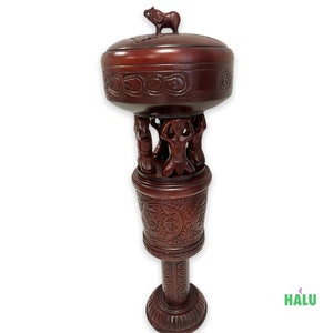 Puede incluir: Una caja de madera de color rojo oscuro con un diseño tallado y una pequeña figura de animal en la tapa. La caja está sobre un alto soporte de madera tallada con cuatro figuras que sostienen la caja.