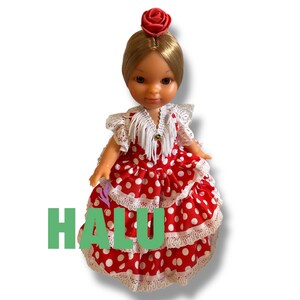 May include: A doll wearing a red and white polka dot dress with white lace trim. The doll has blonde hair and a red rose hair accessory. The word "HALU" is printed in green on the dress.
