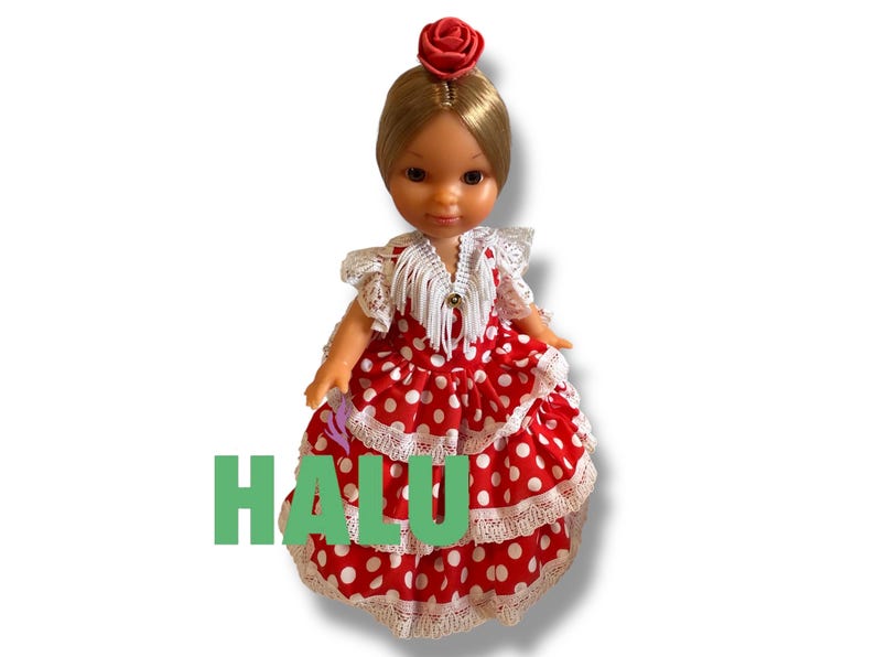 May include: A doll wearing a red and white polka dot dress with white lace trim. The doll has blonde hair and a red rose hair accessory. The word "HALU" is printed in green on the dress.