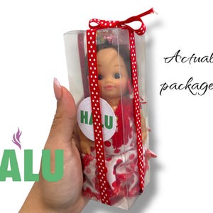May include: A doll in a clear plastic box, tied with a red ribbon with white polka dots. The doll is wearing a red and white dress and has a round sticker with the word "HALU" on it. The text "Actual package!" is written in cursive.