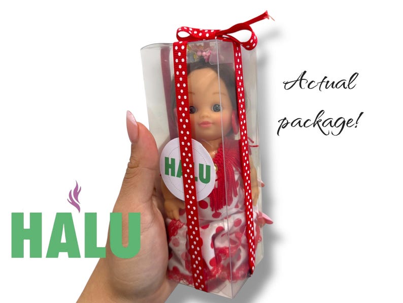 May include: A doll in a clear plastic box, tied with a red ribbon with white polka dots. The doll is wearing a red and white dress and has a round sticker with the word "HALU" on it. The text "Actual package!" is written in cursive.