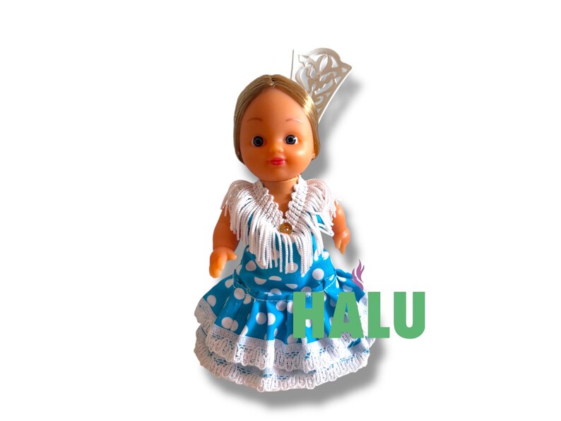 May include: A doll in a blue polka-dot dress with white lace trim and a white fringed shawl. The doll has blonde hair and a decorative headpiece. The word "HALU" is written in green letters.