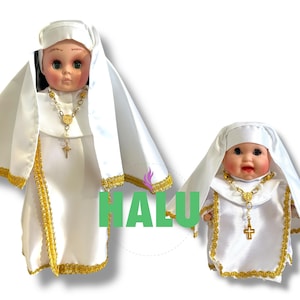 May include: Two white porcelain dolls dressed as nuns. The dolls are wearing white habits with gold trim and gold crosses. The larger doll has a gold necklace with a heart pendant.