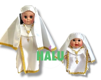 May include: Two white porcelain dolls dressed as nuns. The dolls are wearing white habits with gold trim and gold crosses. The larger doll has a gold necklace with a heart pendant.