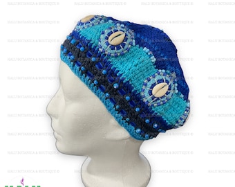 Op de afbeelding: Een blauwe en turquoise gehaakte baret met witte schelpversieringen en blauwe kralen. De baret is op een wit mannequinhoofd.