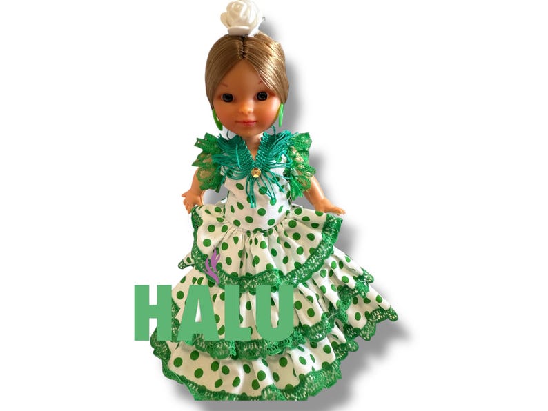 May include: A doll wearing a traditional flamenco dress with white fabric and green polka dots. The dress has ruffled layers and green trim. The doll has brown hair, green earrings, and a white flower in her hair. The word "HALU" is printed in green.