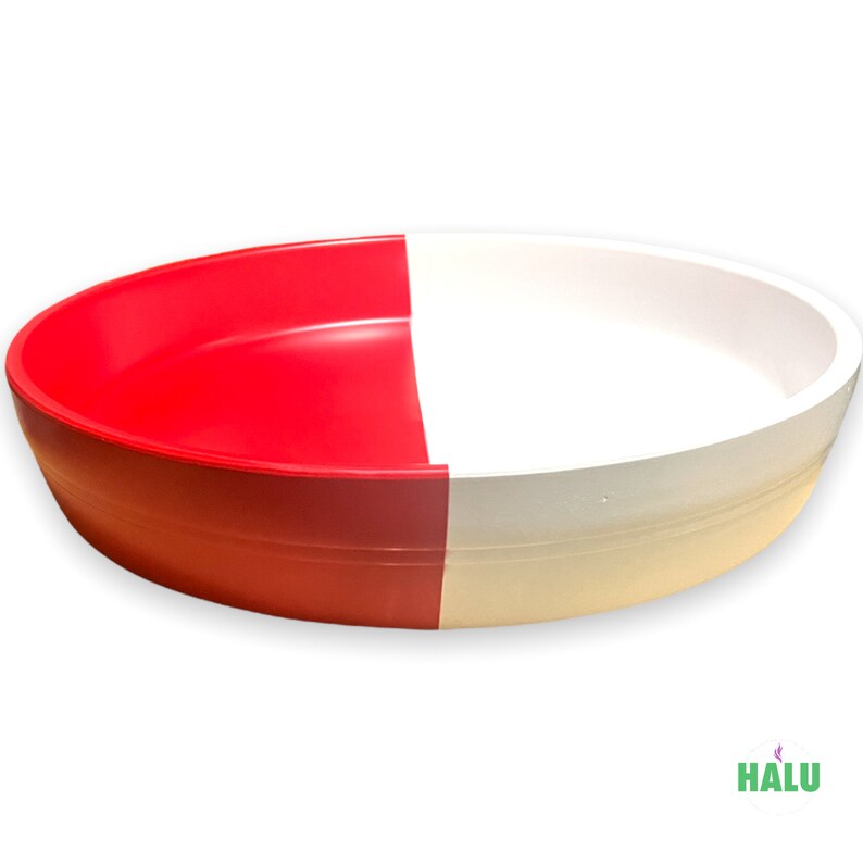 May include: A two-tone, round plastic bowl. One half is bright red, and the other half is white. The bowl has a smooth, glossy finish and a simple, modern design. The bowl is likely used for serving or storage.
