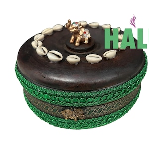 May include: A round, dark brown wooden box with a decorative green trim and a gold elephant figurine on top. The lid is adorned with white seashells. The word "HALU" is printed in green on the right side.