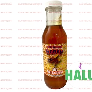 May include: A glass bottle of 100% natural honey labeled "Miel La Reina" with a net weight of 16 oz (1 lb). The bottle has a yellow and orange label with a bee illustration and honeycomb pattern. The label also includes the text "100% Natural Honey".