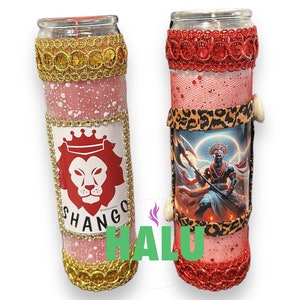 May include: Two red glass candle jars with decorative trim. The left candle jar has a gold trim and a red lion with a crown on a white background. The text "SHANGO" is printed below the lion. The right candle jar has a red trim and a black and white image of a man holding an axe. The text "HALU" is printed in green on the right side of the image.