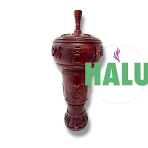 Pode incluir: Um queimador de incenso vermelho escuro e ornamentado com tampa e uma alça decorativa alta. O corpo apresenta desenhos esculpidos e a palavra "HALU" em letras verdes. O queimador está em um fundo branco.