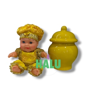 May include: A doll with blue eyes wearing a yellow and gold outfit with a matching hat, positioned next to a glossy yellow ceramic jar with a lid. The doll has a light skin tone and is dressed in a textured yellow fabric with gold trim.