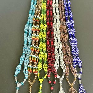 Peut inclure: Un ensemble de huit colliers de perles avec des glands. Les colliers sont faits de perles de verre de différentes couleurs, notamment bleu, vert, jaune, rouge, blanc et marron. Les glands sont faits de perles de la même couleur.