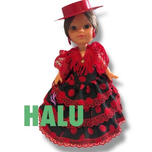 May include: A doll wearing a red hat and a traditional Spanish flamenco dress. The dress is black with red polka dots and lace trim. The word "HALU" is printed in green on the dress.