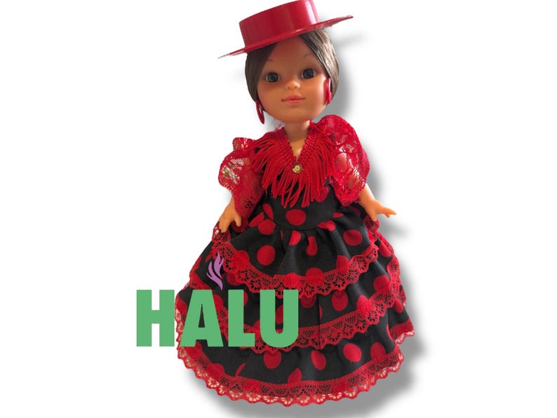 May include: A doll wearing a red hat and a traditional Spanish flamenco dress. The dress is black with red polka dots and lace trim. The word "HALU" is printed in green on the dress.
