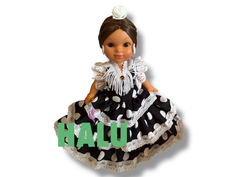 May include: A doll wearing a black and white polka dot dress with white lace trim. The doll has brown hair, a white flower hair accessory, and white earrings. The word "HALU" is written in green letters on the dress.