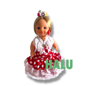 May include: A doll in a red and white polka dot dress with a white lace trim. The doll has blonde hair, a flower hairpiece, and a white shawl. The word "HALU" is printed in green on the dress.