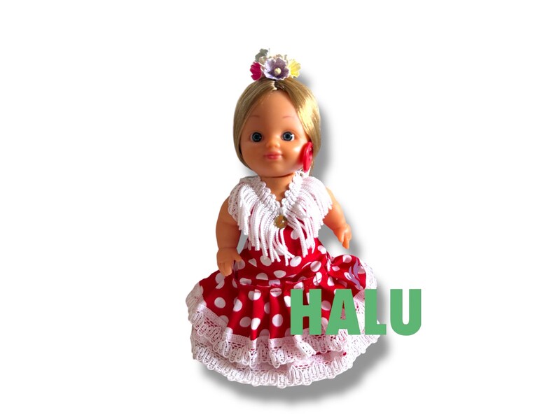 May include: A doll in a red and white polka dot dress with a white lace trim. The doll has blonde hair, a flower hairpiece, and a white shawl. The word "HALU" is printed in green on the dress.