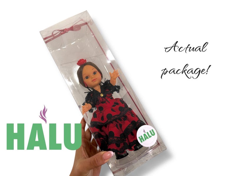 May include: A doll in a clear plastic package. The doll is wearing a red dress with black polka dots and lace trim. The doll has brown hair and a red flower in her hair. The package has the text "Actual package!" and a logo that says "HALU".