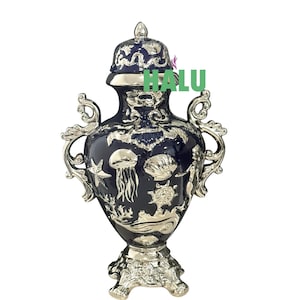 May include: A navy blue and silver decorative urn with a lid. The urn features silver accents of marine life, including a jellyfish, starfish, and seashells. The urn has two ornate handles and a decorative base. The text "HALU" is visible on the urn.