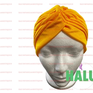 May include: A yellow turban style head wrap made of soft fabric. The turban is folded and tied in a knot on top of the head.