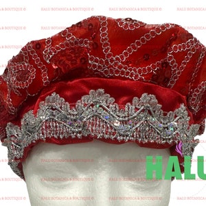 Può includere: Un turbante in raso rosso con ricami e paillettes argentate. Il turbante è piegato e ha un bordo decorativo.