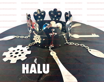Op de afbeelding: Een zilveren kroon met hartvormige uitsnijdingen en een ketting met decoratieve bedels. De kroon bevindt zich op een zwarte achtergrond met het woord "HALU" in wit gedrukt.