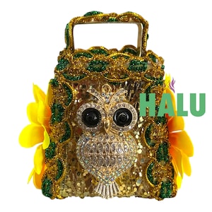 May include: A gold sequined handbag with an owl emblem. The bag has a handle and is decorated with green and gold accents, and yellow flowers. The word "HALU" is printed on the side.