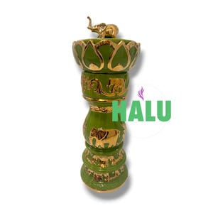 Puede incluir: Un recipiente cilíndrico alto de cerámica verde con motivos de elefantes dorados y patrones de volutas ornamentales. La sección superior tiene forma de flor de loto y está rematada con una pequeña figura de elefante dorada. El texto HALU es visible.