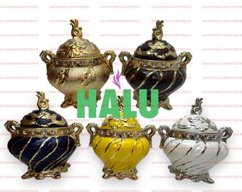 Pode incluir: Cinco potes decorativos com tampa, duas alças e acabamento dourado ou prateado. Os potes possuem acabamento brilhante em dourado, castanho escuro, azul marinho, amarelo e branco, com strass transparentes e um puxador decorativo.