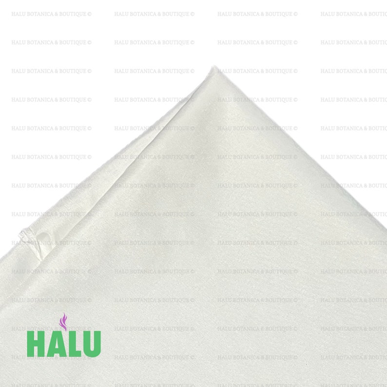 May include: A white satin fabric square with a folded corner. The fabric is smooth and has a slight sheen. The fabric is folded in half and the corner is folded over to create a triangle shape. The fabric is lying flat on a white surface. The text "HALU" is printed in green on the fabric.
