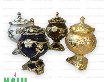 Pode incluir: Quatro potes de cerâmica decorativos com tampas. Os potes são de diferentes cores: branco, azul, marrom e dourado. Cada pote tem desenhos dourados intrincados e pedras brilhantes.