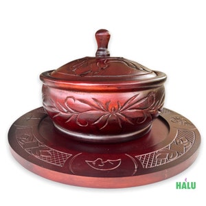 Puede incluir: Un cuenco de madera de color rojo oscuro con tapa y base a juego. El cuenco y la base están tallados con intrincados diseños florales.