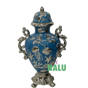 May include: A blue decorative urn with a lid, featuring silver accents and handles. The urn is adorned with sea-themed designs, including jellyfish, starfish, and seashells. The base and lid are also silver.
