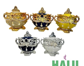 Pode incluir: Cinco tigelas decorativas com tampa em ouro, azul marinho e amarelo, com detalhes florais e de cristal ornamentados. As tigelas têm alças e assentam em bases decorativas. O logotipo "HALU" está no canto inferior direito.