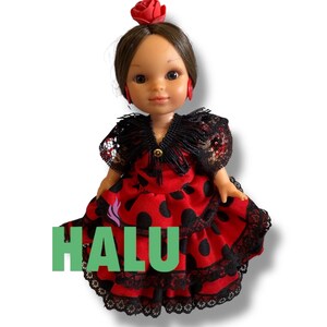 May include: A doll wearing a red dress with black polka dots and black lace trim. The doll has brown hair, red earrings, and a red rose in her hair. The word "HALU" is printed in green on the dress.