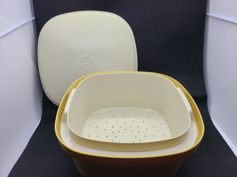 May include: A yellow plastic steamer with a white lid and a removable white strainer insert. The lid has the word "Tupperware" printed on it.