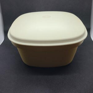 May include: A white square-shaped plastic container with a lid. The container has a smooth surface and a slightly rounded bottom.