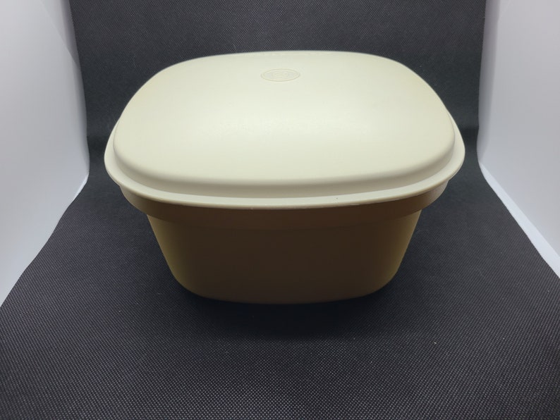 May include: A white square-shaped plastic container with a lid. The container has a smooth surface and a slightly rounded bottom.
