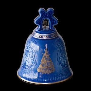 Puede incluir: Una campana de cerámica azul con detalles dorados que representa una iglesia y el texto "Stavkirk - Lerdal" y "Untwisst Bells".