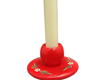 May include: A cream-colored candle sits in a red wooden candle holder. The candle holder has a round base with floral and leaf designs. The candle holder is a decorative item.
