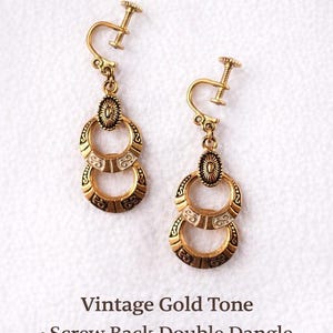 Könnte beinhalten: Vintage goldfarbene Ohrringe mit Schraubverschluss und doppeltem Anhänger. Jeder Ohrring hat zwei verzierte, ineinandergreifende Reifen mit einem ovalen Akzent. Die Ohrringe sind nicht durchbohrt.
