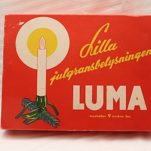 Puede incluir: Una caja roja con una ilustración blanca y amarilla de una vela en un árbol de Navidad. La caja dice "Lilla julgransbelysningen LUMA" y "Innehåller 9 stycken ljus".